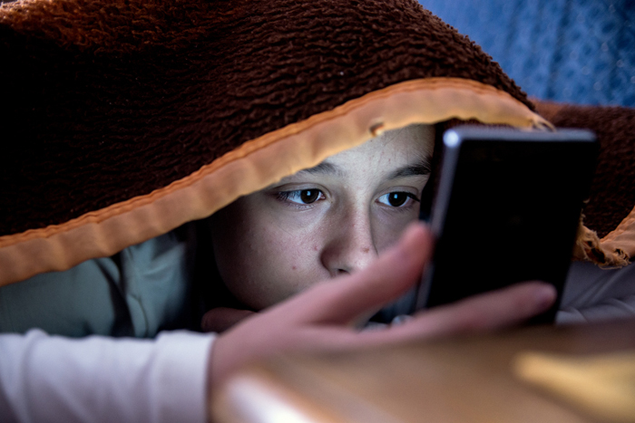 child under blanket viewing a mobile device